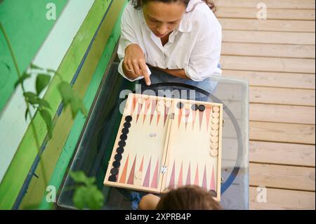 Eine Frau genießt ein Spiel Backgammon mit einem Freund im Freien. Die Umgebung ist ungezwungenermaßen, was auf Freizeit und Freundschaft hinweist. Stockfoto