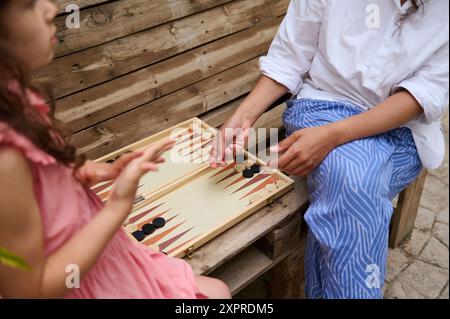 Mutter und Tochter spielen im Freien Backgammon, während sie auf einer Holzbank sitzen. Ein Moment voller Spaß, Verbundenheit und Entspannung. Stockfoto