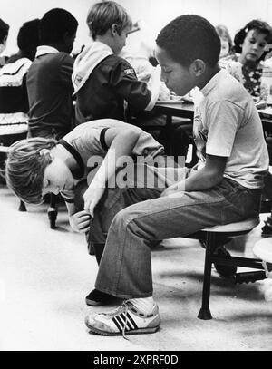 Austin Texas USA, 1984: Patrick Skeaton, der sein rechtes Bein wegen Spina bifida verlor, interagiert mit einem neugierigen Klassenkameraden in der Schulcafeteria der Wooten Elementary. Später wurde er mit einer Beinprothese ausgestattet. Teil einer erweiterten Fotofunktion. ©Bob Daemmrich Stockfoto