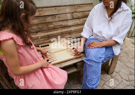 Mutter und Tochter verbringen gute Zeit miteinander und spielen draußen ein Spiel Backgammon. Das Bild fängt einen verbindenden Moment und die Freude der Familie lei ein Stockfoto