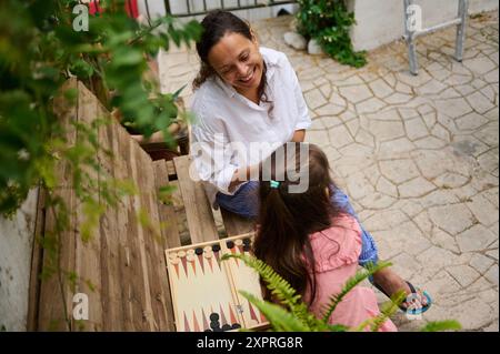 Eine Mutter und Tochter, die einen freudigen Moment teilen, während sie draußen Backgammon in einer ruhigen Umgebung spielen. Die Szene fängt das Wesen der Familienbindung ein Stockfoto