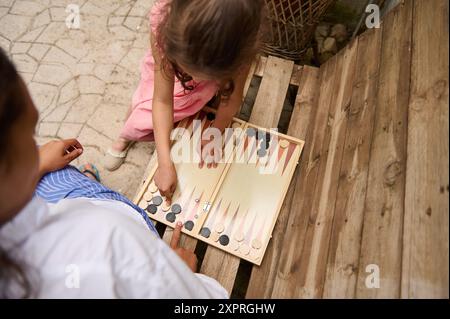 Mutter und Tochter genießen gute Zeit, indem sie draußen Backgammon spielen. Das Bild fängt einen Familienmoment voller Spaß und Verbundenheit ein. Stockfoto
