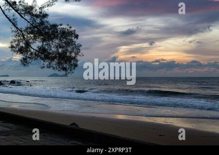 Silhouette eines Baumzweigs über Wellen, die vom Südchinesischen Meer zum Damai Beach in Sarawak, Malaysia, eindringen Stockfoto