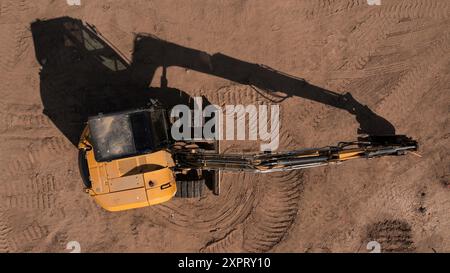Geradlinige Ansicht eines Baggers auf einer Ebenen Baustelle mit Profilspuren im Sand. Stockfoto