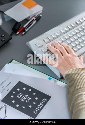 Eine Person, die auf einer Computertastatur im FRONTEX-Lagezentrum in Warschau tippt, mit einem Dokumentenordner für EU-Bürger auf dem Schreibtisch. Das Bild repräsentiert Überwachung, Grenzkontrolle und Koordinierung durch die Europäische Union. Stockfoto