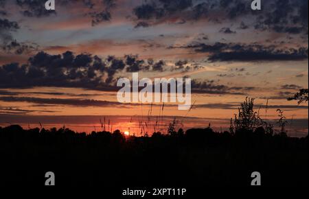 Nach einem warmen Tag strahlt die Sonne ein orangenes Leuchten aus, das die Wolken hervorhebt, während sie über der West Lancashire Ebene nahe Hoscar untergeht. Stockfoto