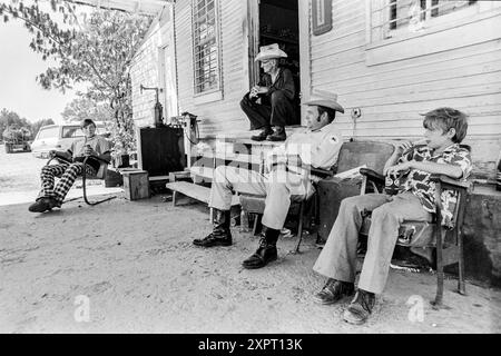 Mazedonien, Arkansas, USA – 23. Juni 2024: Horizontale Aufnahme von Freunden, die vor einem alten Laden aus den 1970er Jahren sitzen und sich unterhalten. Stockfoto