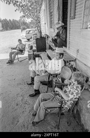 Mazedonien, Arkansas, USA – 23. Juni 2024: Vertikale Aufnahme von Männern und Jungen, die vor einem Landhaus aus den 1970er Jahren in Arkansas sprechen. Stockfoto