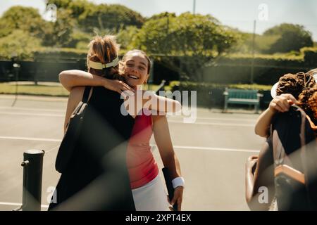 Eine Gruppe von Tennisspielerinnen, die sich auf dem Tennisplatz umarmen und feiern und Freundschaft und Freude nach einem Spiel zum Ausdruck bringen Stockfoto
