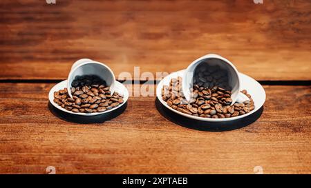 Zwei Keramikbecher verschütten geröstete Kaffeebohnen auf einer rustikalen Holzoberfläche, die die reichhaltige Textur und Farbe der Bohnen zum Ausdruck bringt Stockfoto