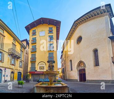 BERGAMO, ITALIEN - 7. APRIL 2022: Fassade der Kirche San Pancrazio und mittelalterliches Haus mit Sonnenuhr hinter dem Brunnen San Pancrazio in Citta Alta (U Stockfoto