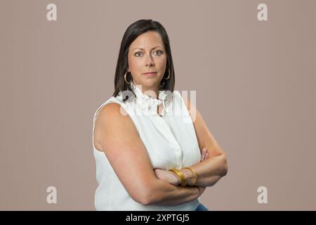 Kopfaufnahme einer kaukasischen brünetten Geschäftsfrau mittleren Alters im Studio auf beigefarbenem Hintergrund mit überkreuzten Armen Stockfoto