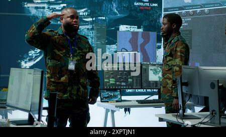 Militärangehörige betreiben fortschrittliche Systeme in einer Kommandozentrale, die sich auf Überwachung und Datenanalyse zum Schutz der nationalen Sicherheit konzentrieren. Soldaten, die ausgebildet sind, um Informationskriege zu verwalten. Kamera A.. Stockfoto
