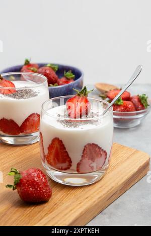 Zwei Gläser Erdbeer-Joghurt-Parfait mit Chiasamen, serviert mit frischen Erdbeeren in Schüsseln auf einem Holzbrett. Stockfoto