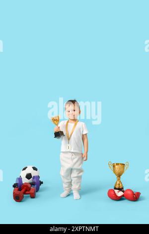 Niedlicher kleiner Athlet mit erster Medaille, goldenem Cup und Sportausrüstung auf blauem Hintergrund Stockfoto