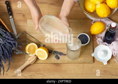 Junge Frau, die Zitronensaft aus der Kanne in Glas gießt, um Lavendellimonade auf Holztisch zuzubereiten Stockfoto