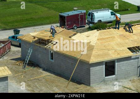 Professionelle Bauarbeiter, die an der Dachkonstruktion eines unvollendeten Vorstadthauses mit Holzrahmenstruktur im ländlichen Gebiet Floridas arbeiten. Wohnungskonzept Stockfoto