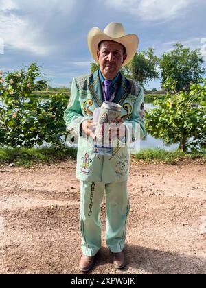 Jhon Smith Noriega posiert am 14. Juli 2024 für ein Porträt neben dem oberen Kanal in der Laguna del Nainari in der Stadt Obregón, Sonora, Mexiko. Jhon trägt ein Kostüm der beliebten oder regionalen Musikgruppe La Banda namens lLaberinto und bittet um finanzielle Unterstützung mit einem Boot mit dem Bild der Jungfrau von Guadalupe für „Mi Casa Albergue“ (Foto: Luis Gutiérrerez / Norte Photo) Jhon Smith Noriega posa para un retrato junto al Canal alto en la Laguna del Nainari en ciudad Obregón Sonora México el 14 julio 2024. Jhon viste de traje de la agrupación de músical Popular o Regional de la Banda Stockfoto