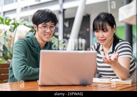 Zwei junge asiatische Studenten schauen sich einen Laptop-Bildschirm an, diskutieren über die Arbeit und machen gemeinsam ein Projekt in einem Café in der Stadt. Stockfoto