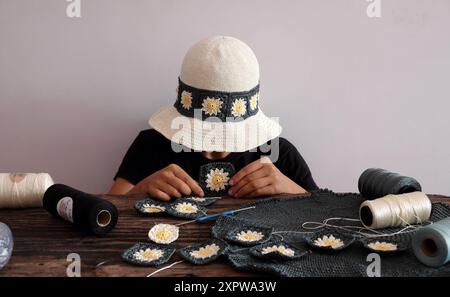 Frauen tragen Gänseblümchenmotive Häkelhut, umgeben von einer Vielzahl von farbenfrohen Materialien für diy-Projekte, Freizeit mit Kreativität handgefertigt in Workspa Stockfoto