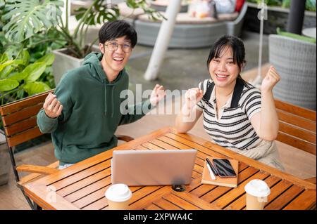 Zwei fröhliche, freundliche junge asiatische Freundinnen sitzen draußen an einem Tisch, zeigen ihre Faust und lächeln vor die Kamera und feiern Stockfoto