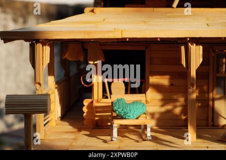 Diese Miniatur-Veranda-Szene hat einen rustikalen Charme. Es verfügt über ein Puppenhaus, helles Holz, ein Strohdach und gemütliche Liegestühle mit Türkis Stockfoto