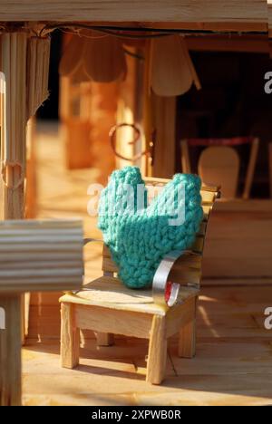 Diese Miniatur-Veranda-Szene hat einen rustikalen Charme. Es verfügt über ein Puppenhaus, helles Holz, ein Strohdach und gemütliche Liegestühle mit Türkis Stockfoto