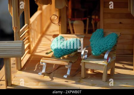 Diese Miniatur-Veranda-Szene hat einen rustikalen Charme. Es verfügt über ein Puppenhaus, helles Holz, ein Strohdach und gemütliche Liegestühle mit Türkis Stockfoto