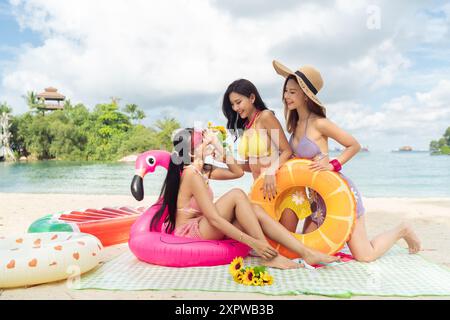 Drei asiatische Freundinnen genießen ein tropisches Picknick am Strand Stockfoto