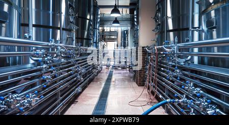 Elegantes, modernes Brauereiinnere mit Reihen glänzender Edelstahltanks, die durch komplexe Rohrleitungssysteme verbunden sind und eine effiziente Bierproduktion betonen. Stockfoto