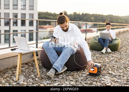 Geschäftsmann, das Telefon auf dem Dach mit tragbarem Kraftwerk auflädt Stockfoto