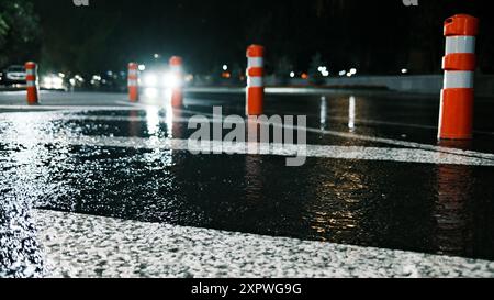 Nasser schwarzer Asphalt in der Nacht mit Plastikpfollern Stockfoto