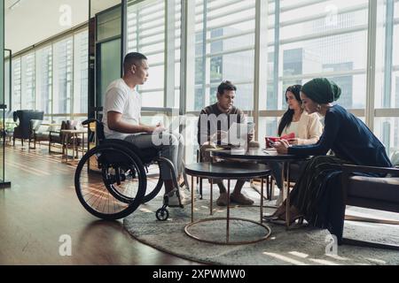 Verschiedene asiatische Geschäftsleute, darunter ein behinderter Mann im Rollstuhl, bei einem zwanglosen Meeting Stockfoto