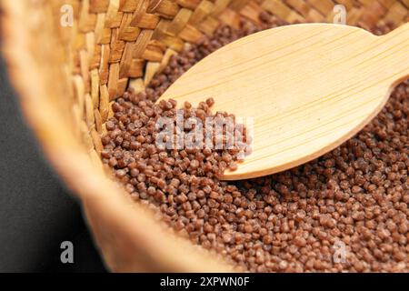 Rohe Buchweizen-Couscous-Körner im Bambuslöffel in geflochtener rustikaler Schüssel. Makroaufnahme Stockfoto