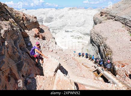 Ein junges Mädchen mit Hut auf dem Kopf und Frontino im Rucksack, während es im Sommer einen sehr steilen Pfad zwischen einer Rinne in den hohen Bergen hinabfährt Stockfoto