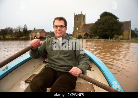 Der Pfarrer John Longuet-Higgins verhandelt Hochwasser aus dem Fluss Severn, um die maroonierte Kirche St. Michael's und All Angel's in Tirley zu überprüfen. Stockfoto