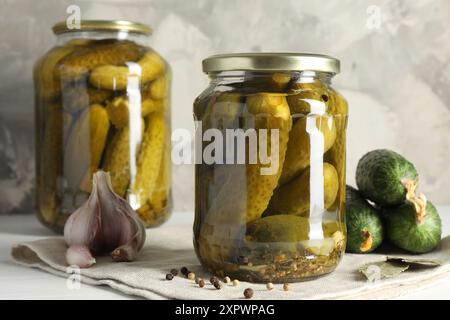 Gurken in Gläsern, frische Gurken und Gewürze auf weißem Tisch Stockfoto
