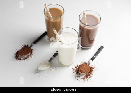 Köstliche Proteinshakes in Gläsern und Löffeln mit Pulver auf weißem Hintergrund Stockfoto