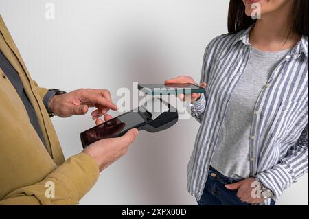 Mitte der weiblichen Kundin, die ihre Rechnung bezahlt, indem sie das Mobiltelefon auf einem Kreditkartenautomaten scannt, der von männlichen Kassierern gehalten wird. Frau und Mann empfehlen Elektro Stockfoto