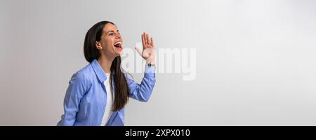 Porträt einer Geschäftsfrau, die ekstatisch schreiend und gestickend im Hintergrund steht. Unternehmerin gekleidet in Business Casuals Stockfoto