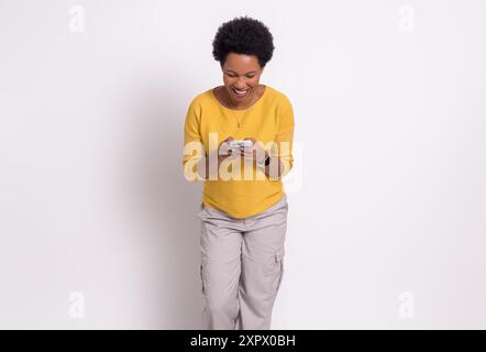 Aufgeregt, glückliche junge Frau in gelbem T-Shirt, die Nachrichten über das Smartphone liest. Fröhliche Frau mit kurzem Afro-Haar Surfnetz auf Handy W Stockfoto