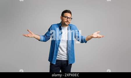 Verwirrter Geschäftsmann, der Hände spreizt und Schultern über grauen Hintergrund zuckt, weiß ich nicht Stockfoto