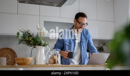 Fröhlicher Geschäftsmann mit Kaffeetasse Videoanruf über Laptop in der Küche im Home Office Stockfoto