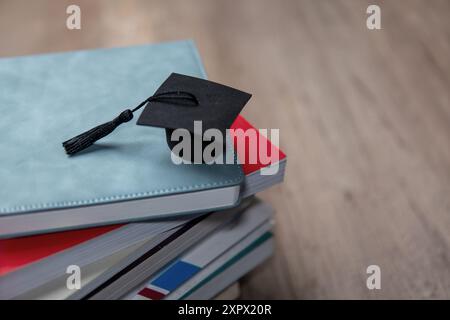 Eine schwarze Graduierungsmütze auf einem Stapel bunter Bücher. Kopierbereich für Text. Bildungs- und Wissenskonzept. Stockfoto