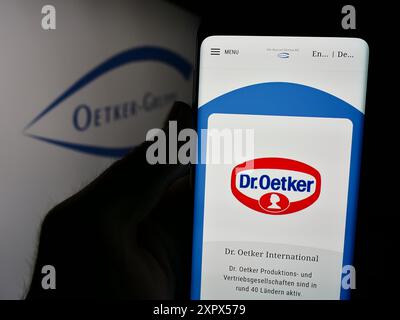 Handyhalter mit Webseite des deutschen Lebensmittelunternehmens Dr. August Oetker KG vor Logo. Konzentrieren Sie sich auf die Mitte des Telefondisplays. Stockfoto