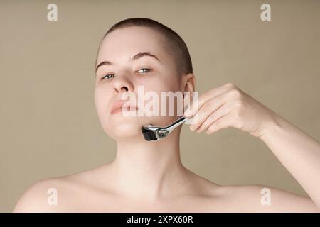 Nahporträt einer jungen Frau mit Dermaroller, die Hautpflege auf neutralem Hintergrundkopierraum genießt Stockfoto