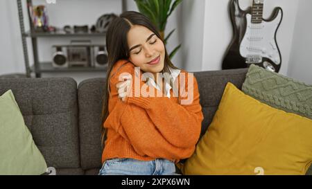 Eine zufriedene junge Frau genießt einen gemütlichen Moment zu Hause, halb geschlossene Augen, die sich auf einem grauen Sofa umarmt Stockfoto