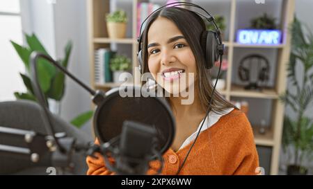 Eine lächelnde junge hispanische Frau mit Kopfhörern in einem Radiostudio Stockfoto