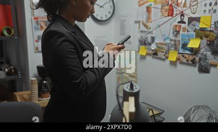 Eine junge hispanische Frau untersucht ein Handy im Büro eines Detektivs, umgeben von Ermittlungsausschüssen und Beweisen. Stockfoto