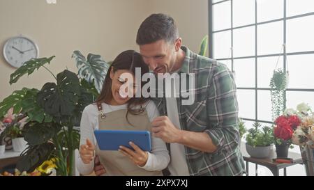 Ein lächelnder Mann und eine lächelnde Frau, beide Floristen, arbeiten in einem lebhaften Blumenladen zusammen und schauen sich ein digitales Tablet an Stockfoto